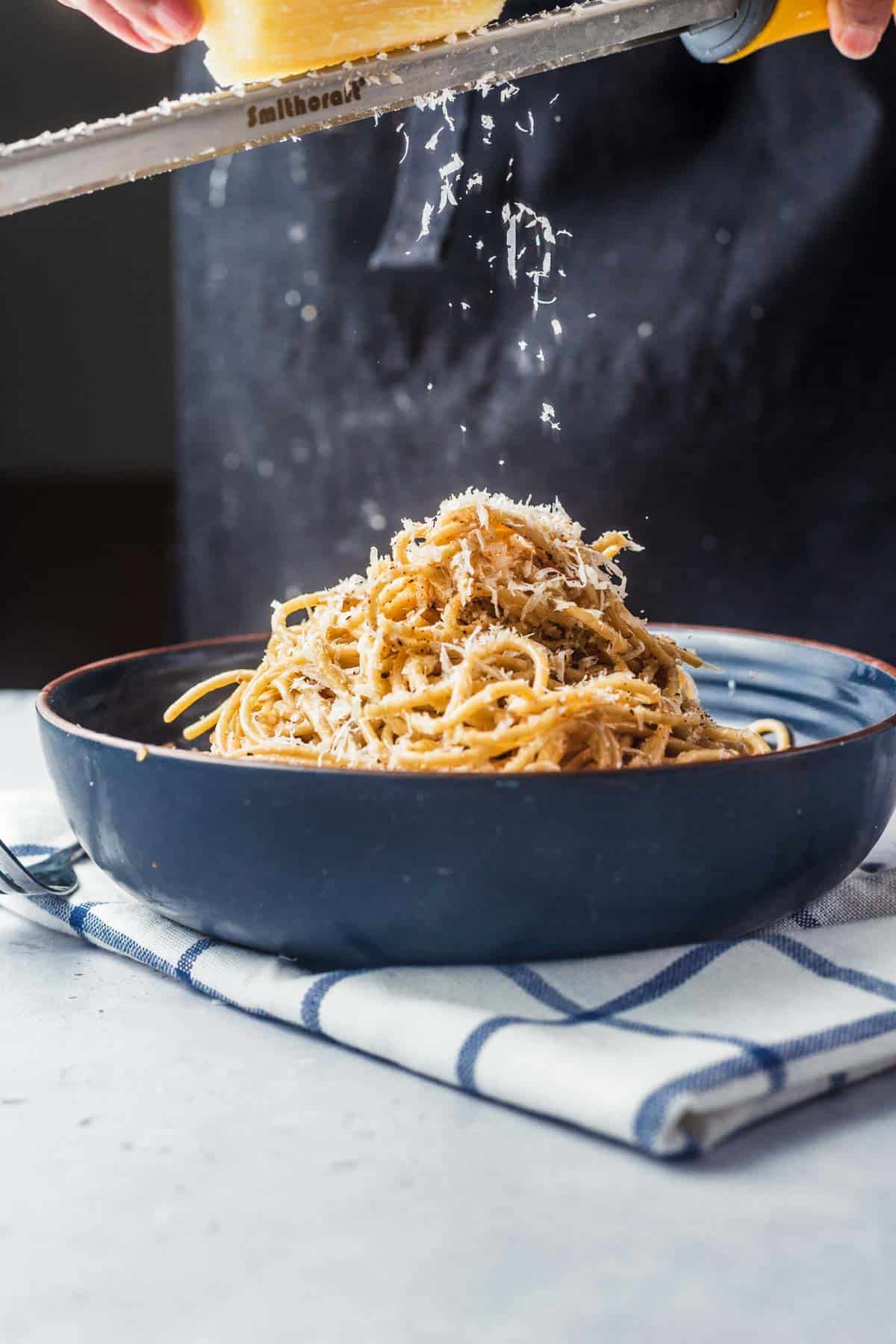 Szechuan Cacio e Pepe in a blue bowl with fresh parmesan cheese grated on top. 