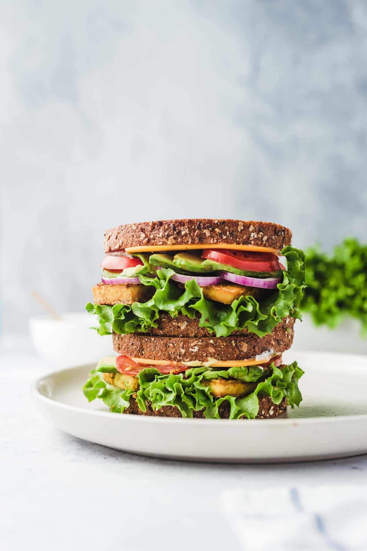 A stacked tofu breakfast sandwich on a white plate. 