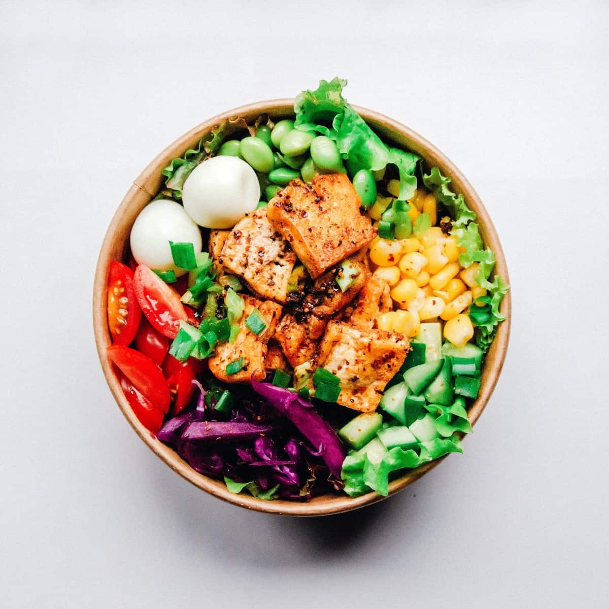 A close up of a tofu salad in a bowl with edamame, cucumber, tomato, corn, and cheese for those following the AB blood type diet.