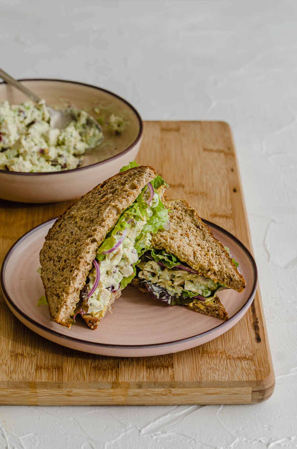 Close up of cranberry chicken salad in a sandwich on a pink plate. 