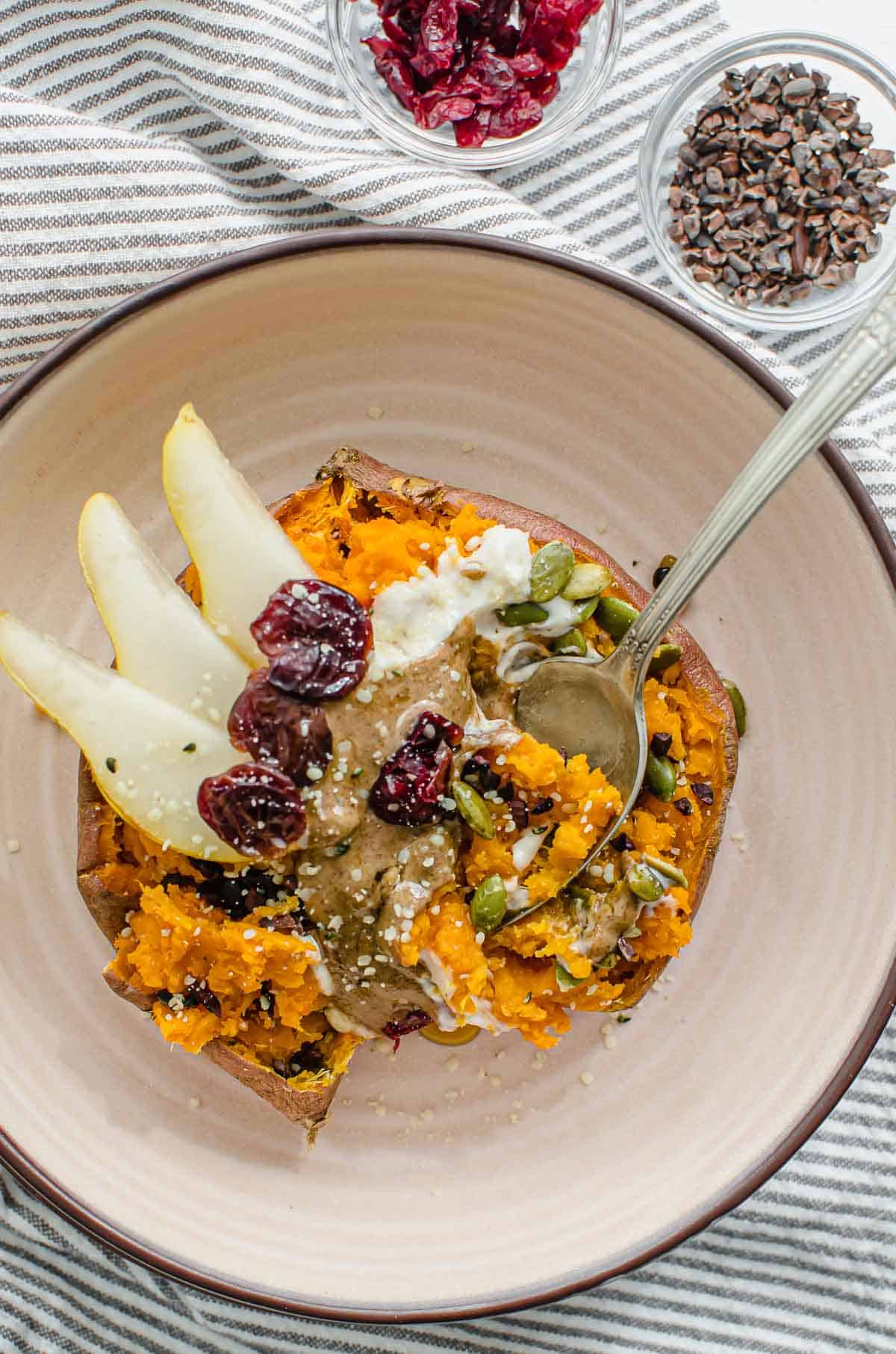 Birds eye view image of sweet potato breakfast bowl with cacao nibs and cranberries on the side. 