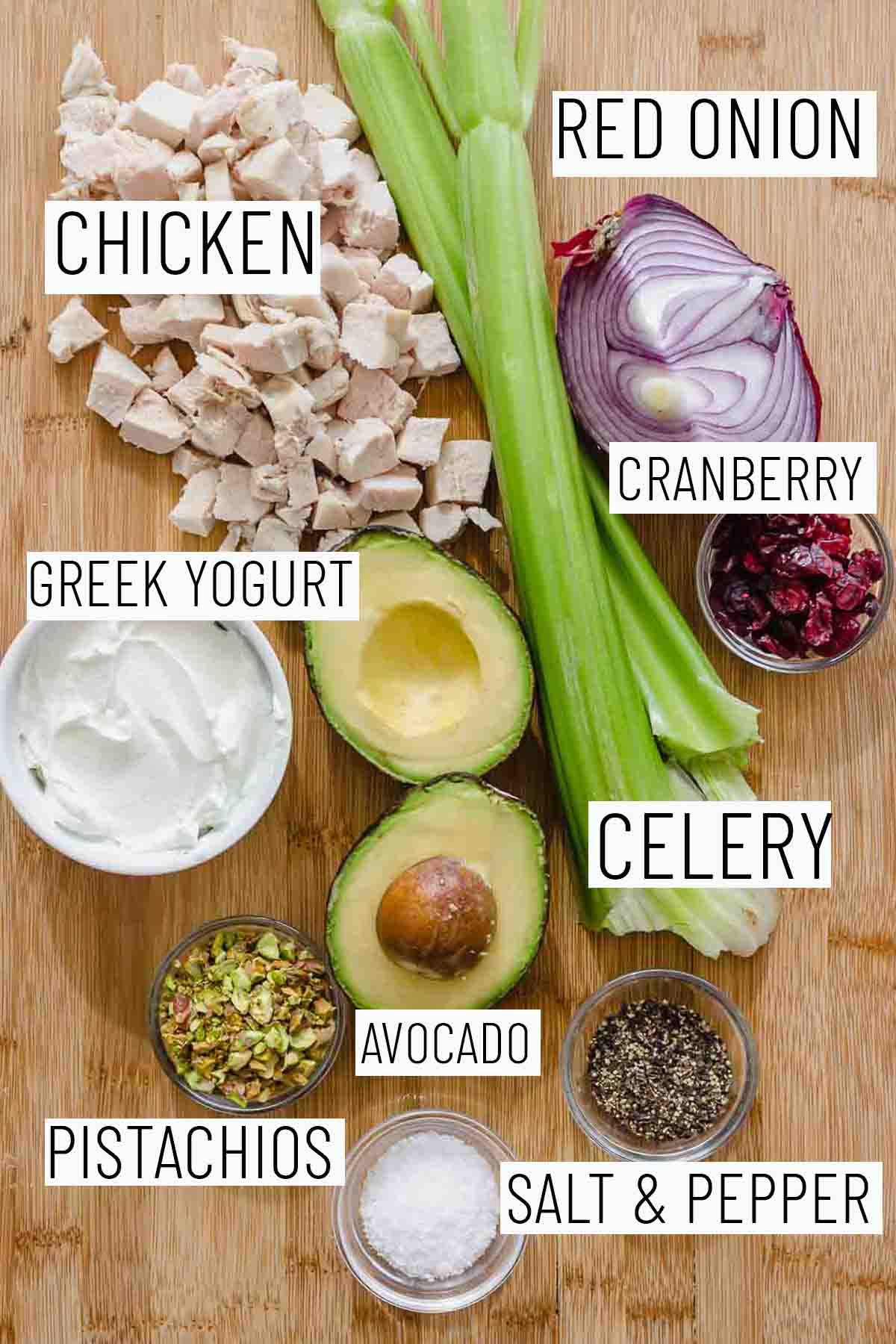 Flat lay image of portioned recipe ingredients including red onion, chicken, cranberry, Greek yogurt, celery, avocado, and pistachio. 