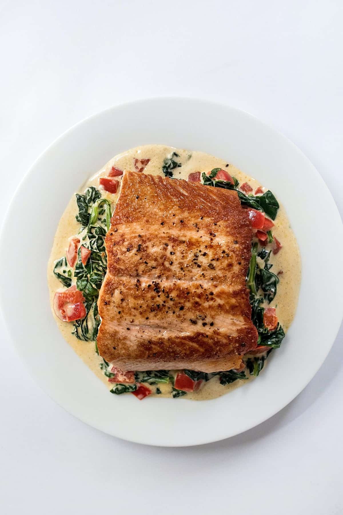 Birds eye view of salmon on a bed of greens in a white plate as an option for those following the type O blood type diet. 