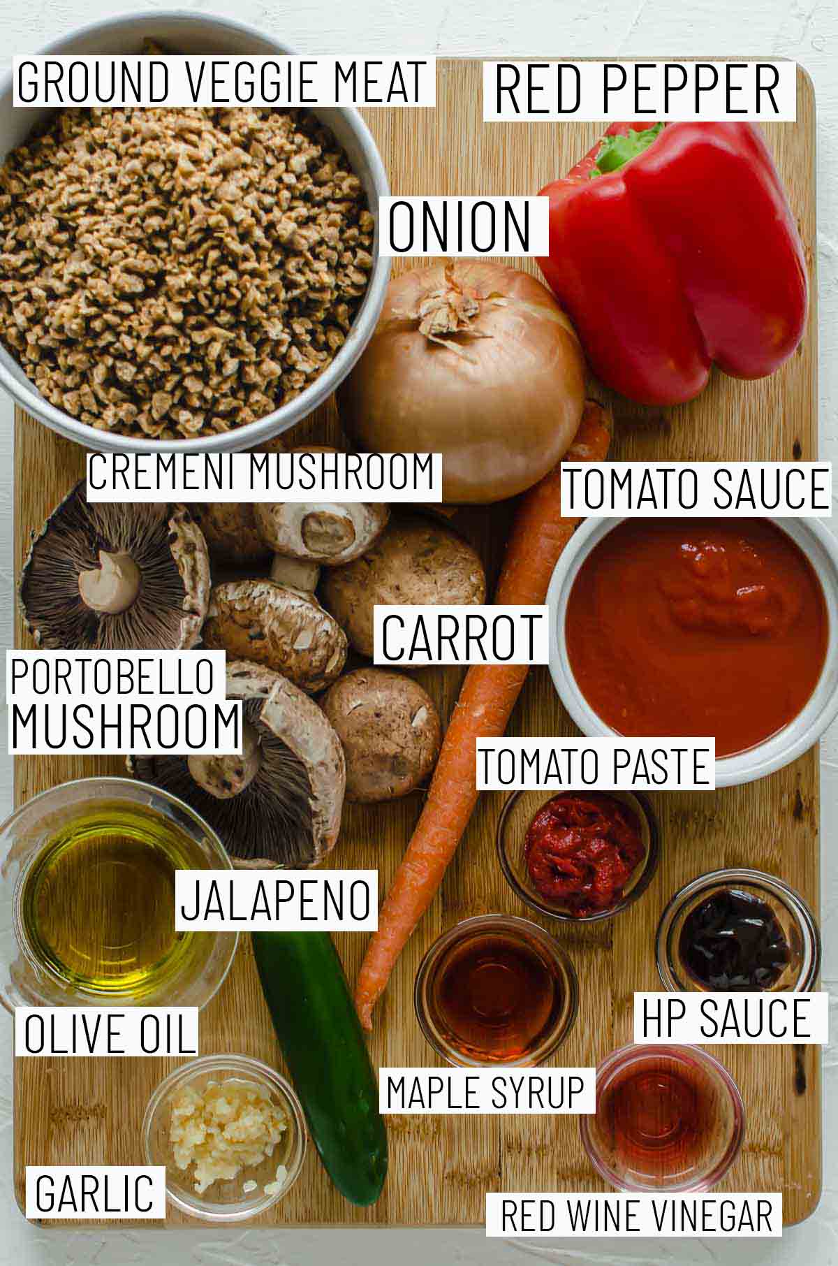 Flat lay image of portioned recipe ingredients including red pepper, onion, veggie meat, tomato sauce, mushrooms, tomato paste, jalapeno, olive oil, garlic, red wine vinegar, HP sauce, and maple syrup.