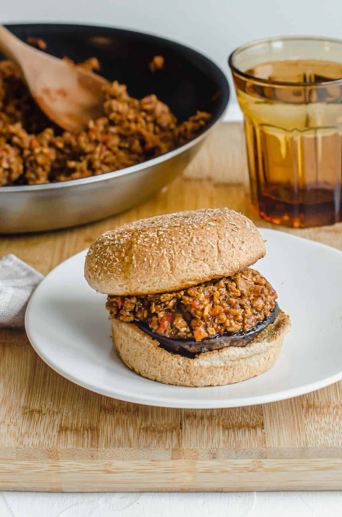 Close up of vegan sloppy joe on a white plate with a glass of water and pan in the background. 