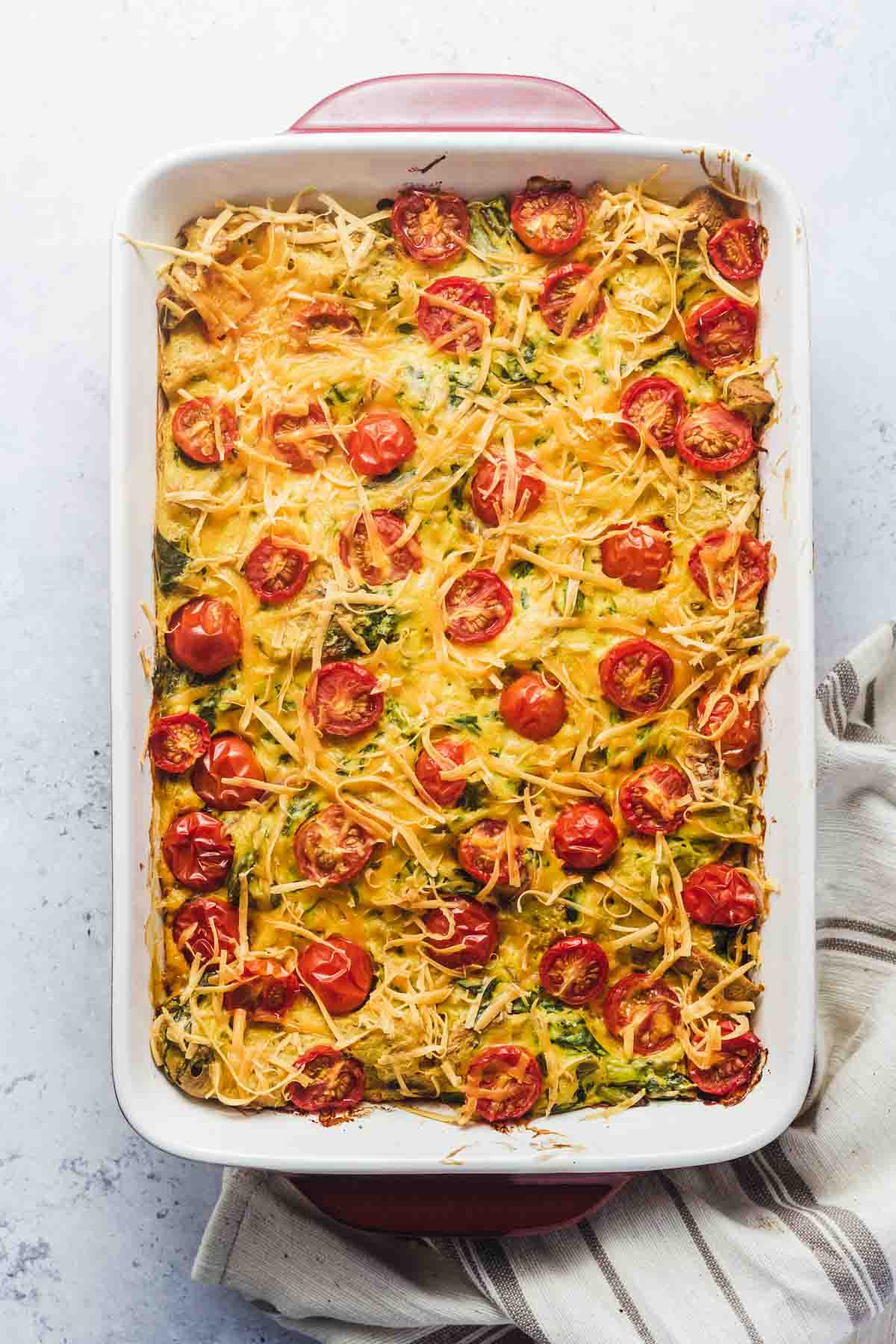 Birds eye view of vegan strata in a casserole dish topped with cheese and tomatoes. 
