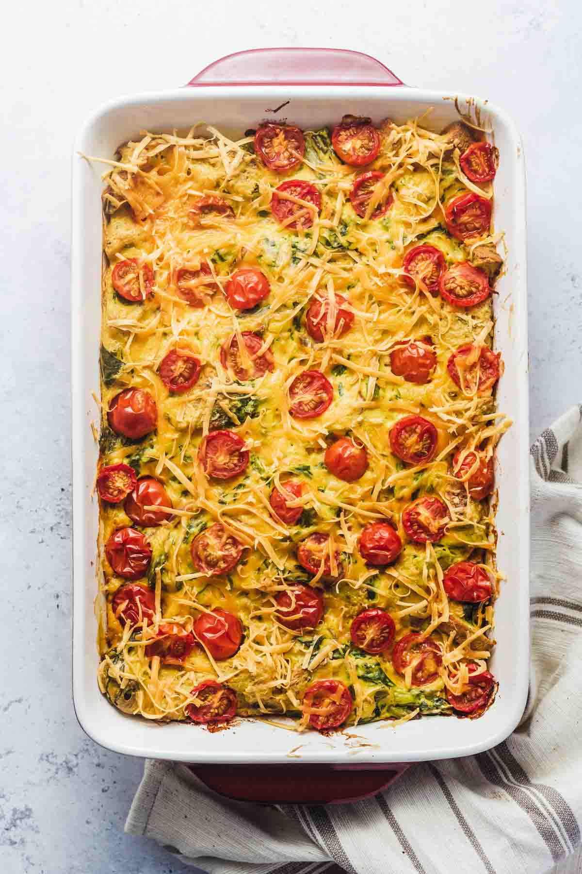 Birds eye view of vegan strata in a casserole dish topped with cheese and tomatoes.