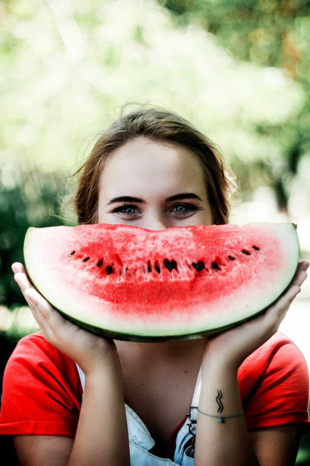 A woman holding up a watermelon in the shape of a smile. 