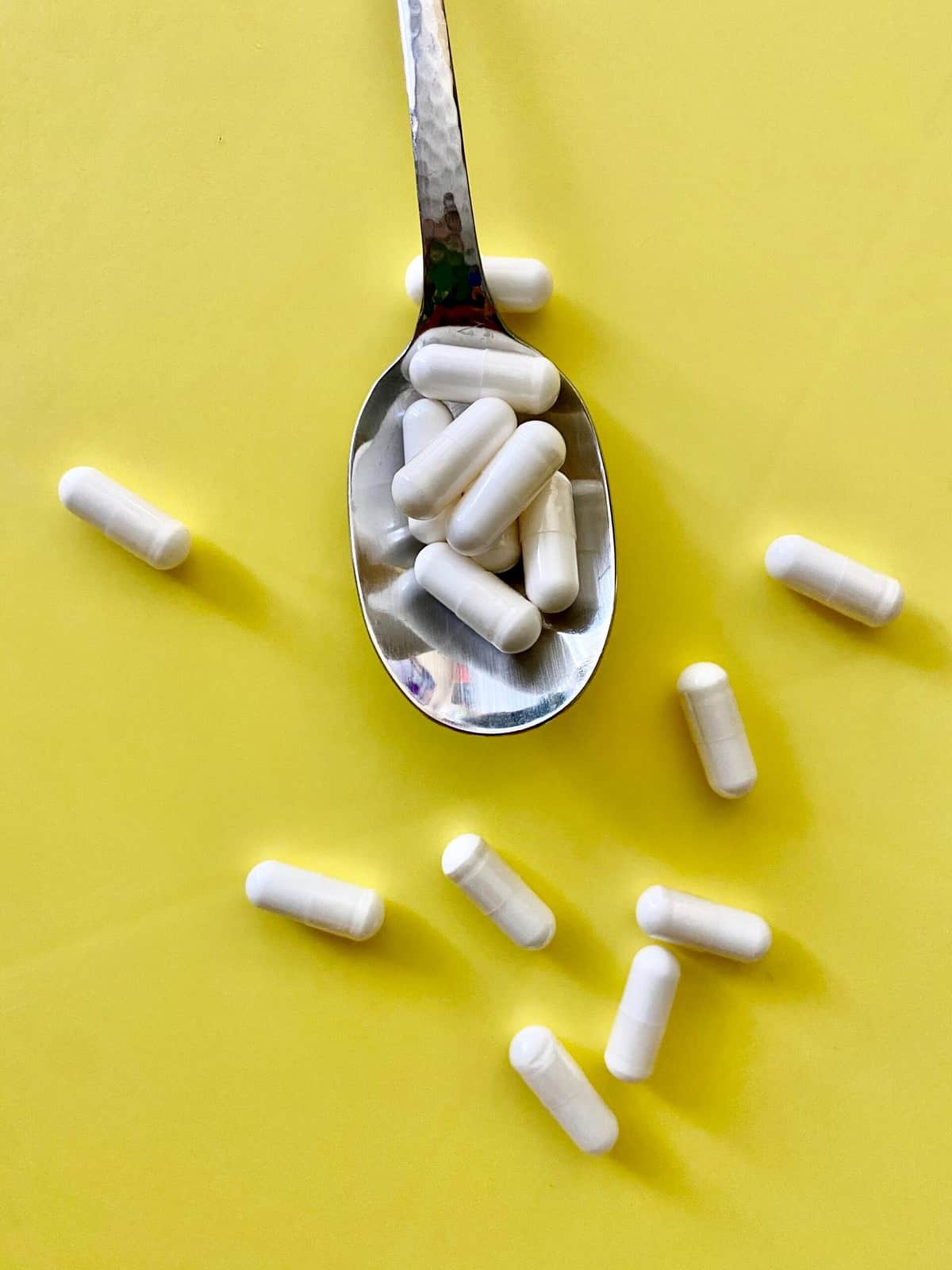 Collagen supplements on a silver spoon against a yellow background.