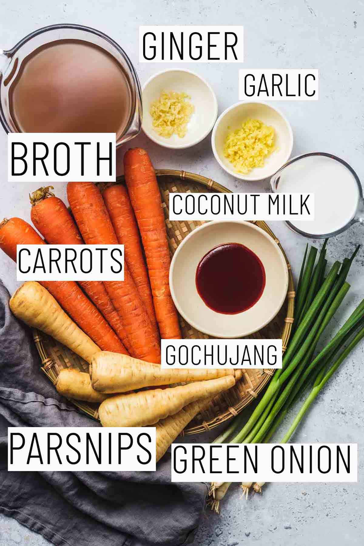 Flat lay image with portioned recipe ingredients including green onion, parsnips, Gochujang, garlic, ginger, broth, and coconut milk.