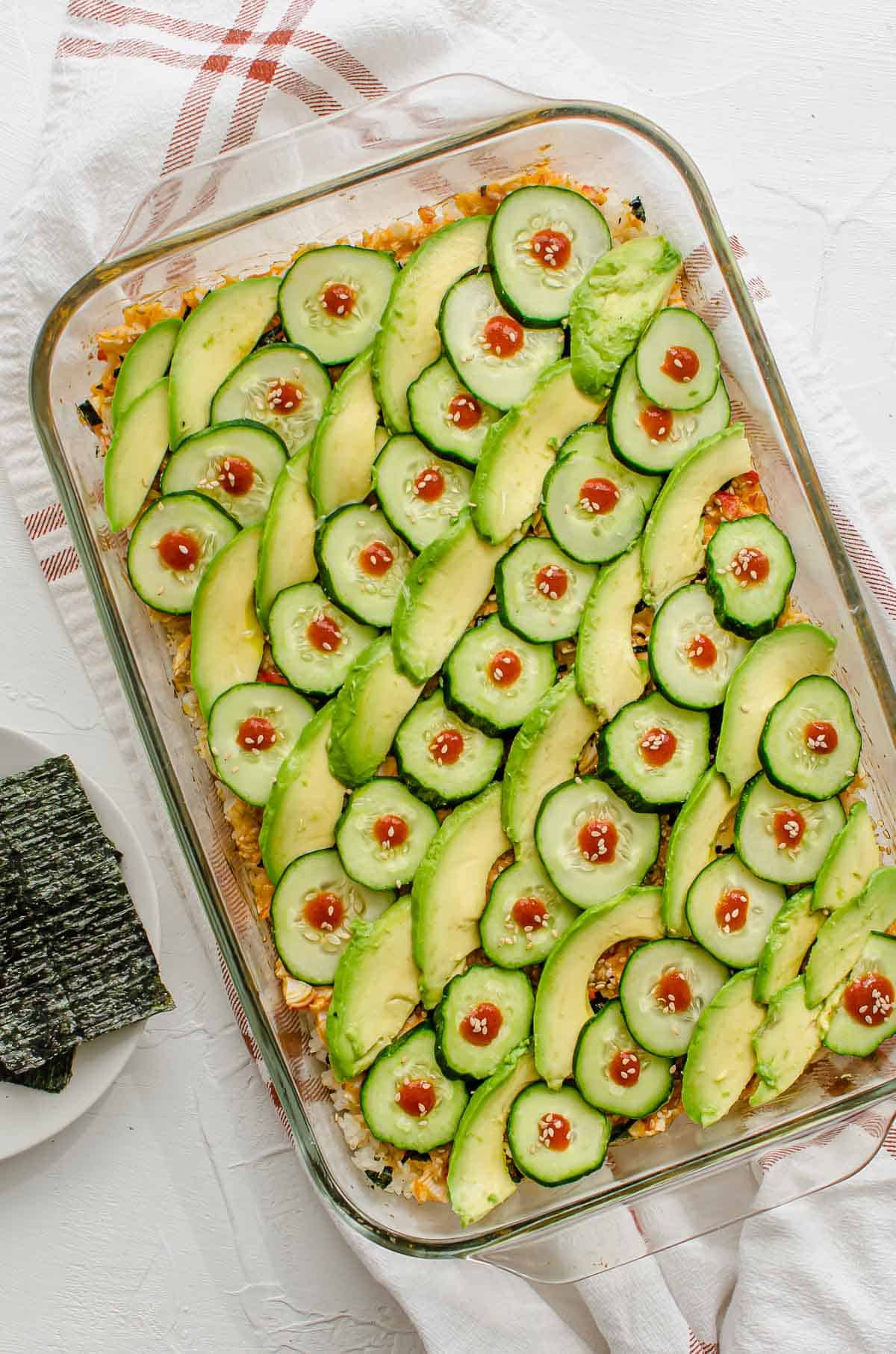 Birds eye view of sushi bake topped with avocado and cucumber.