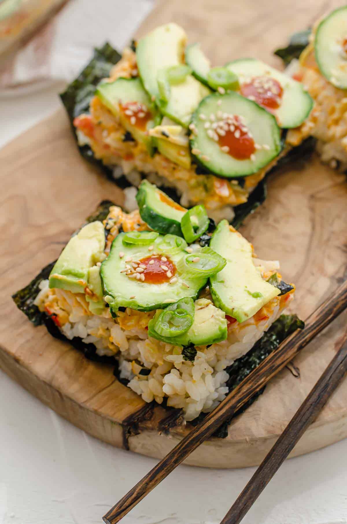 Close up of portioned sushi bake on top of nori sheets and garnished with green onion with chop sticks on the side. 