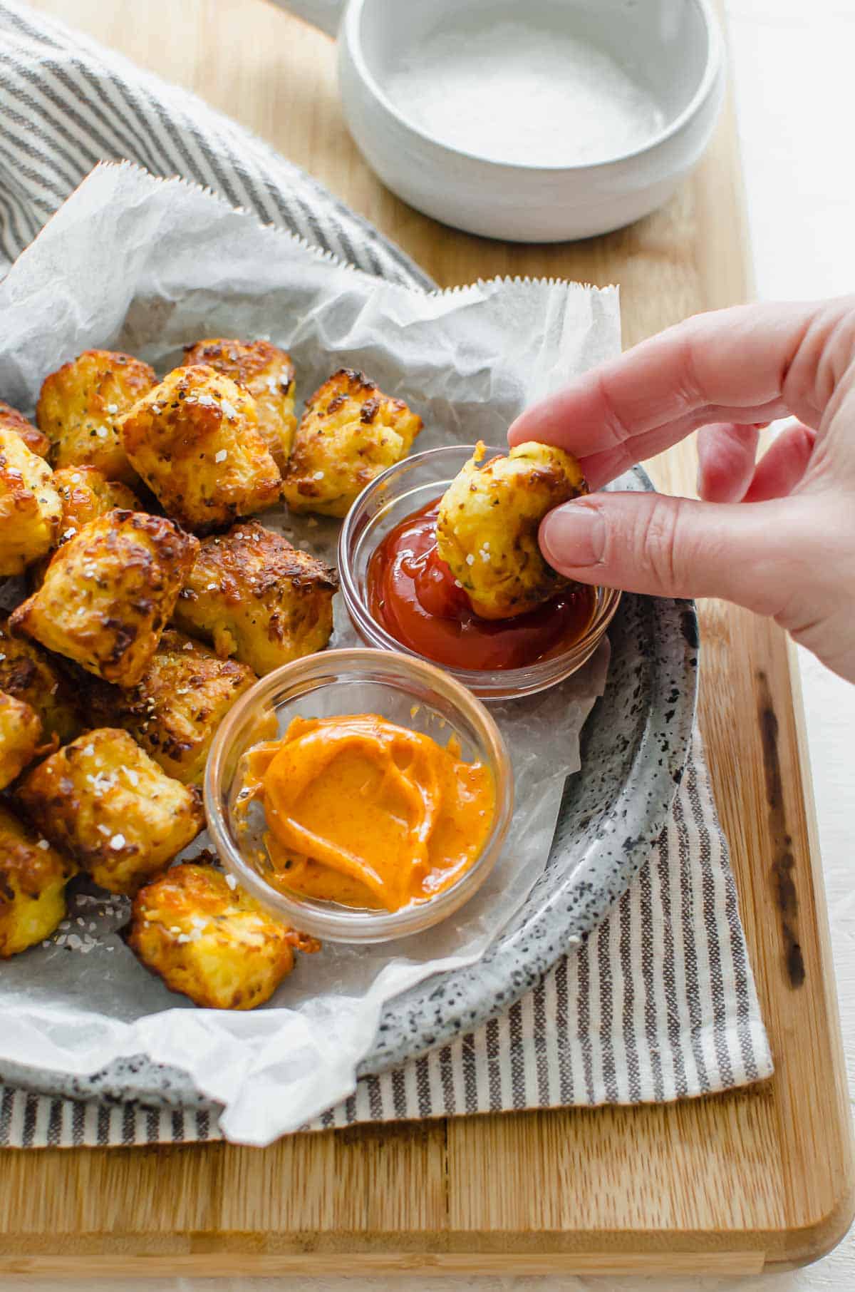 Close up of a hand dipping cauliflower tater tot in ketchup. 