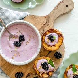 Overhead view of grilled peaches with blackberry sauce inside the middle and a bowl of sauce on the cutting board.