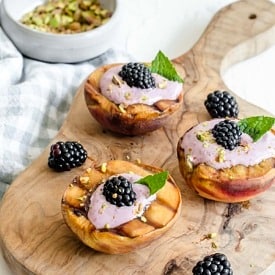 Three grilled peaches with blackberry sauce on a wooden cutting board.