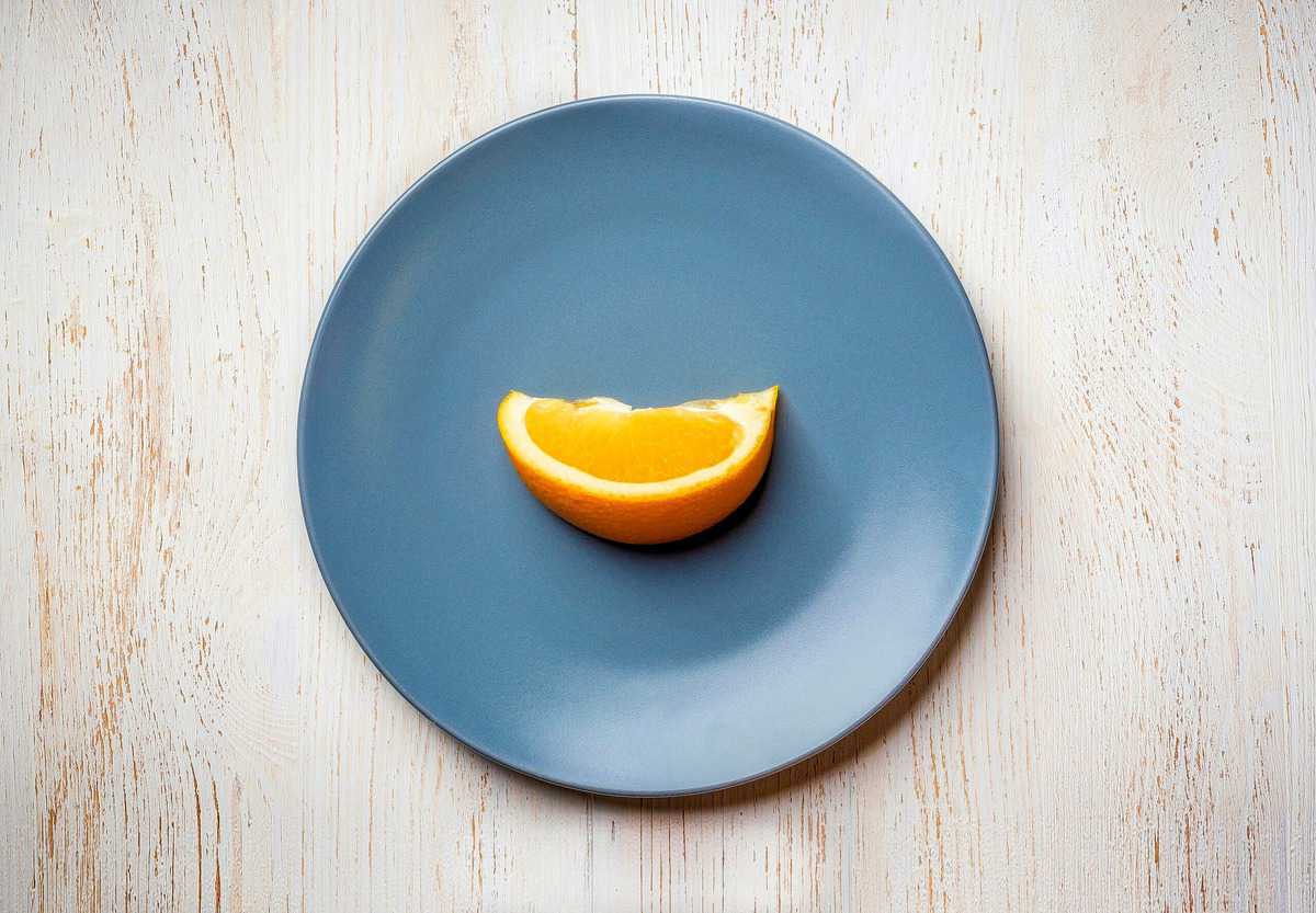 A single orange wedge on a blue plate to show how restrictive intuitive fasting is. 