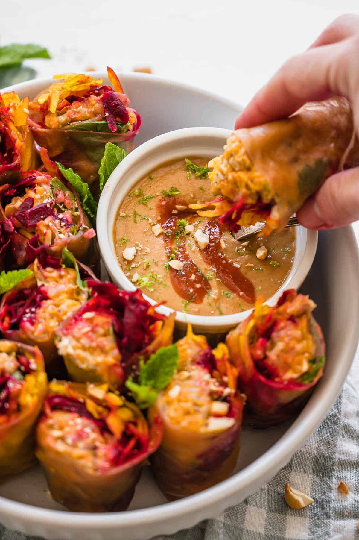 Fresh spring rolls in a bowl, one being dipped into a cashew sauce.