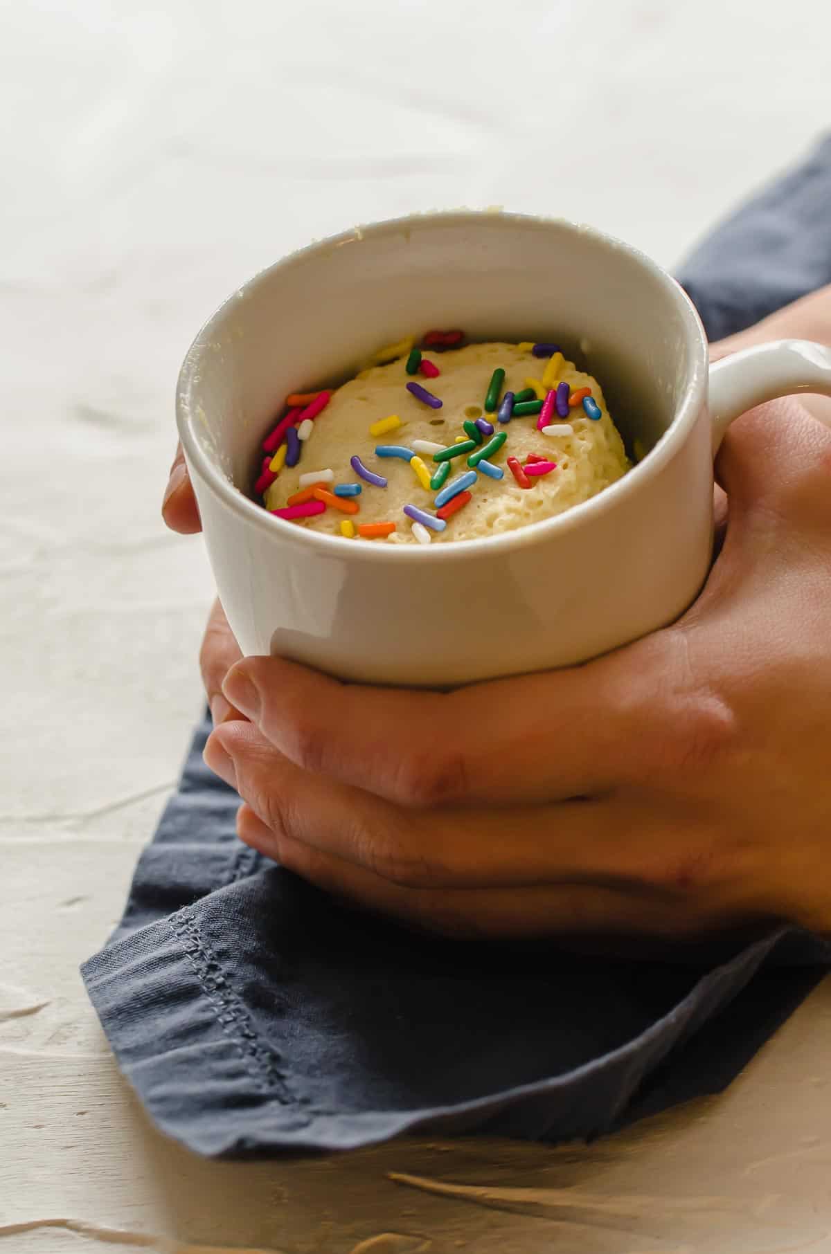 Two hands holding protein mug cake topped with sprinkles. 