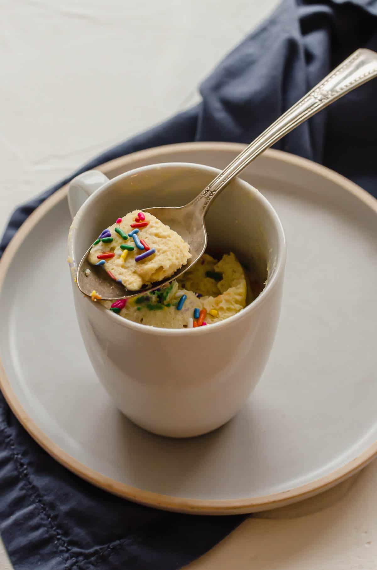 Close up image of protein mug cake in a mug, topped with sprinkles. 