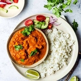 Overhead view of a plate of rice with a bowl of tofu butter chicken alongside garnishes.