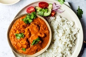 Overhead view of a plate of rice with a bowl of tofu butter chicken alongside garnishes.