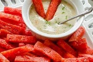 Pinterest graphic of watermelon sticks on a plate with two in dipping sauce.