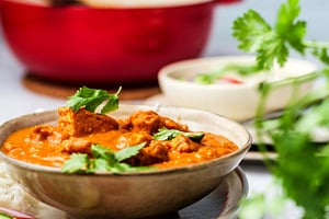 Pinterest graphic of a side profile view of a bowl of vegan butter chicken with a large pot in the background.