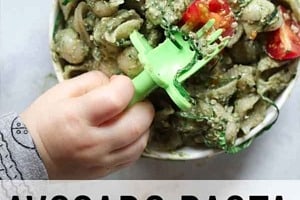 Pinterest graphic of a bowl of avocado pasta with a toddler's hand holding a fork with the overlay text "avocado pasta baby lead weaning."
