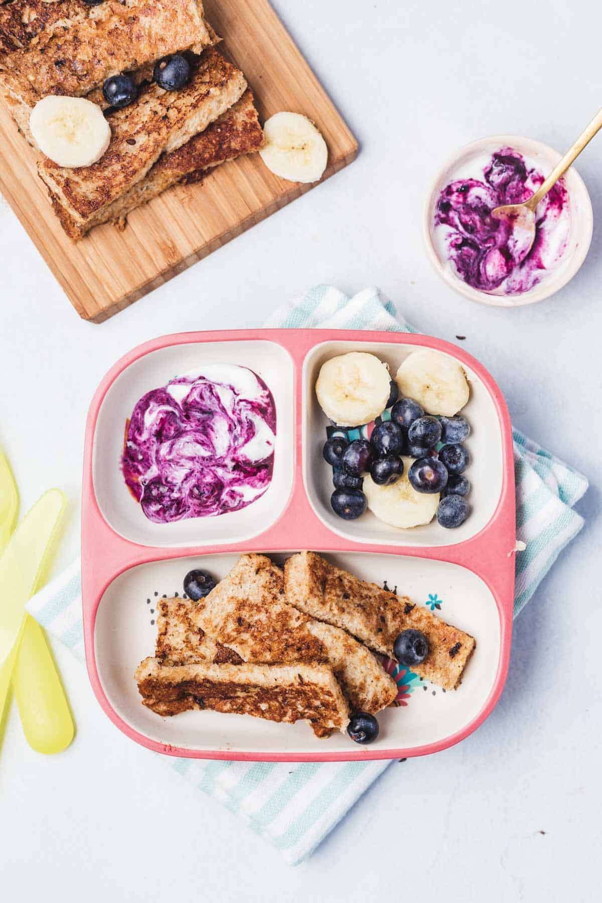 A toddler plate with a section with French toast, a section with fruit, and a section with berry yogurt sauce.