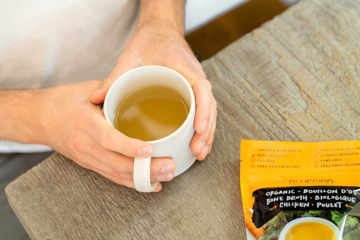 Two hands holding a mug of bone broth.