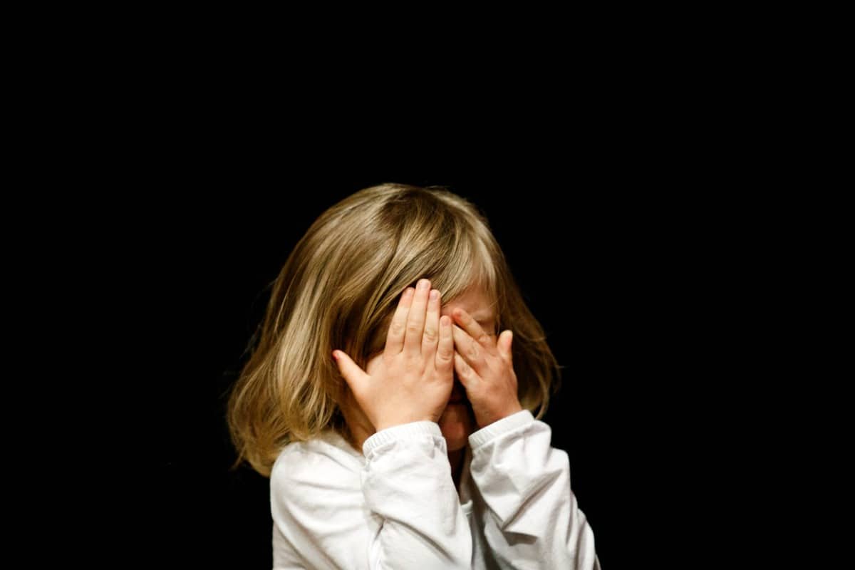 Crying little girl covering her face with her hands.