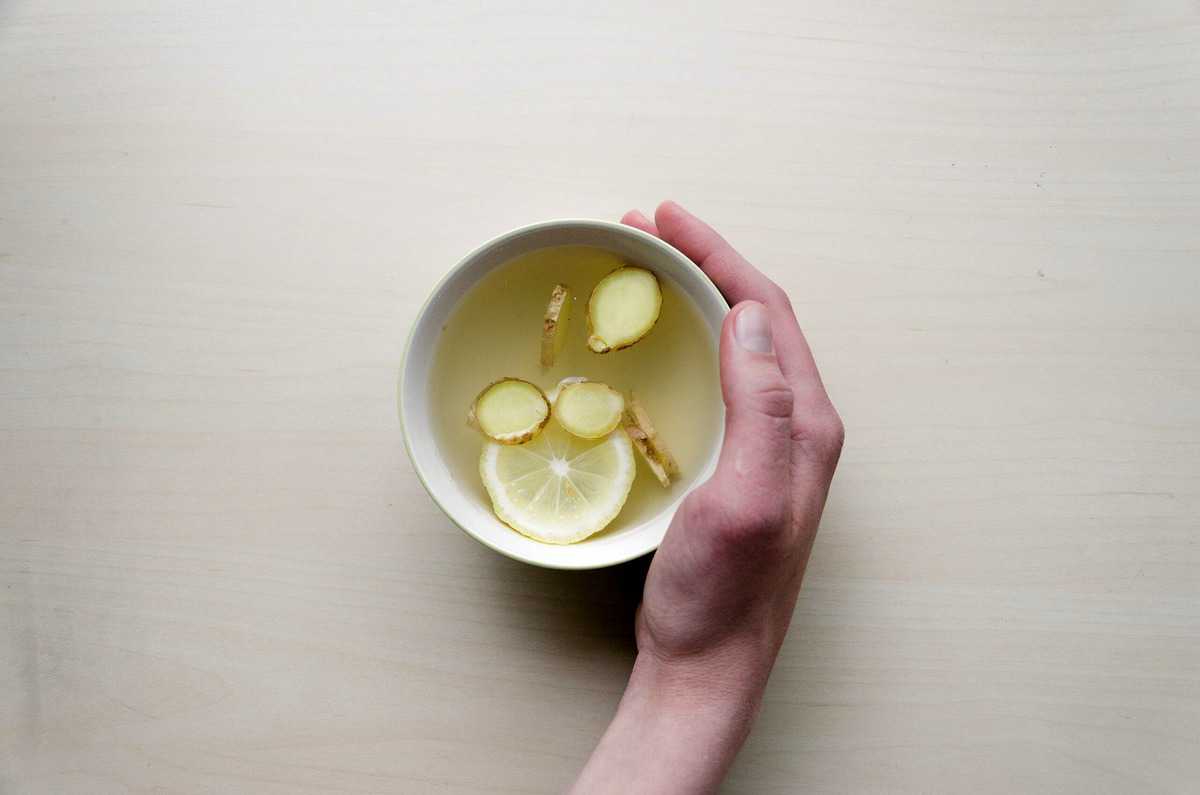 Hand holding a hot lemon and ginger tea.