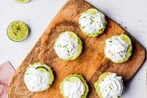 Pinterest graphic of an overhead view of a serving board with multiple mini topped key lime pies with the text overlay "vegan, no-bake key lime pie."