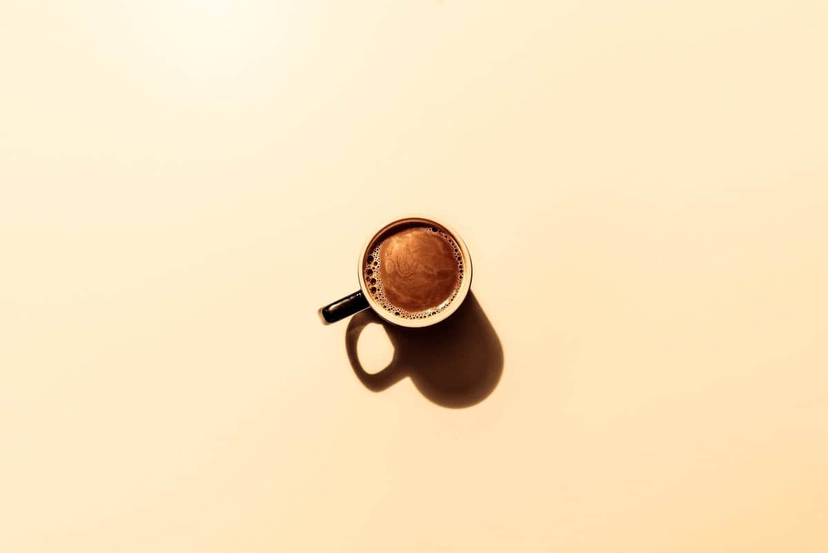 Birds eye view of a cup of coffee against a yellow background.