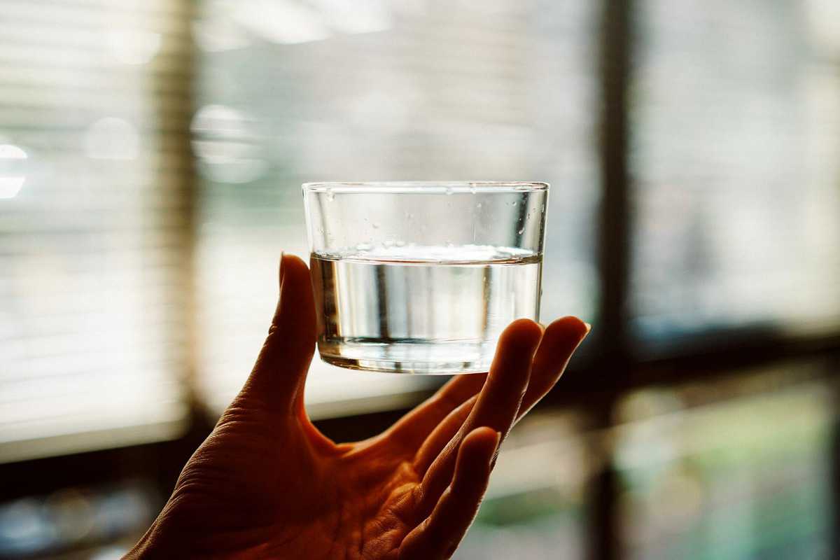 A hand holding up a glass of water for intuitive eating weight loss.