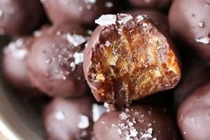 Close up photo of a bowl of Caramel Truffles with Tahini and Dates with one with a bite taken out of it.