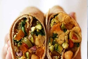 Pinterest graphic of a half holding up a vegan chickpea salad wrap cut in half with the text overlay "easy vegan recipe Moroccan chickpea wrap."