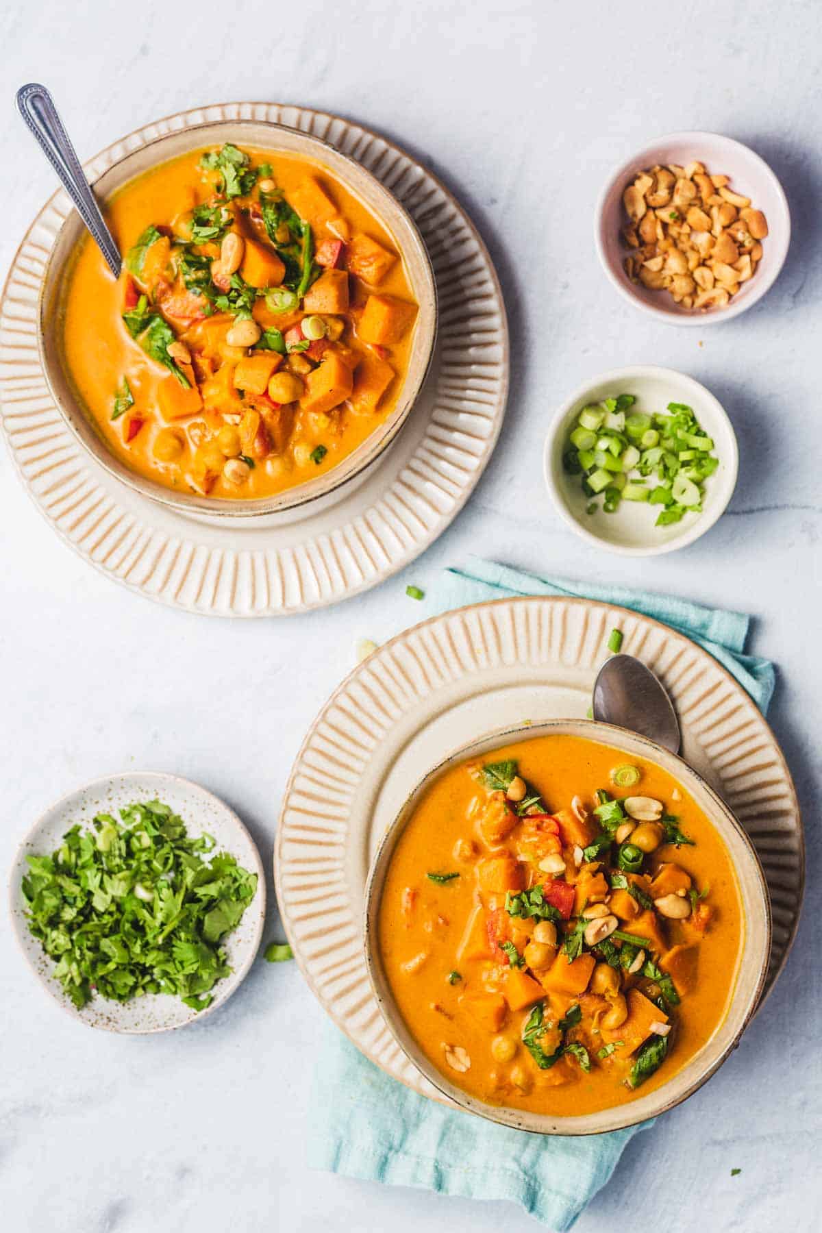 Overhead view of two bowls of sweet potato peanut soup on top of a plate, each. Garnishes on the side in pinch bowls.