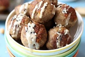 Pinterest graphic of a bowl of toddler meatballs with tahini drizzled on top with the text overlay "Iron Rich BLW Meatballs with Hummus."