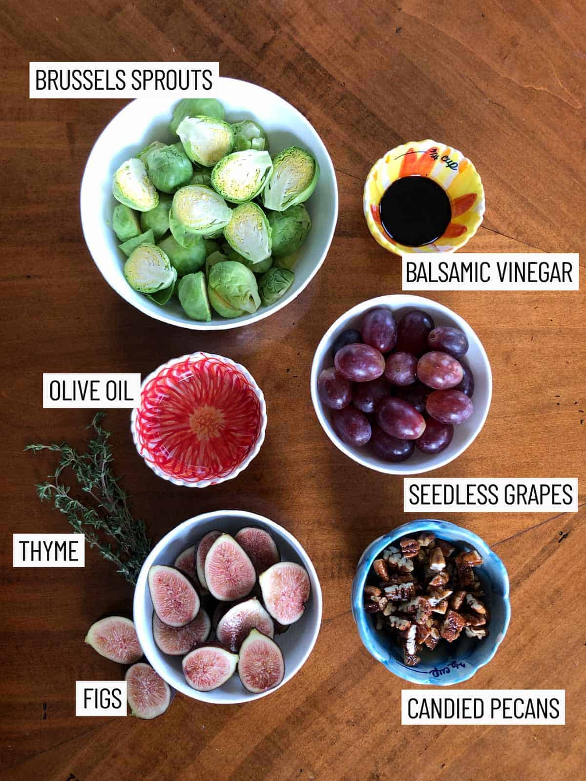 Overhead image of ingredients for Oven roasted balsamic brussels sprouts recipe including Brussels sprouts, balsamic vinegar, olive oil, seedless grapes, thyme, figs, and candied pecans.