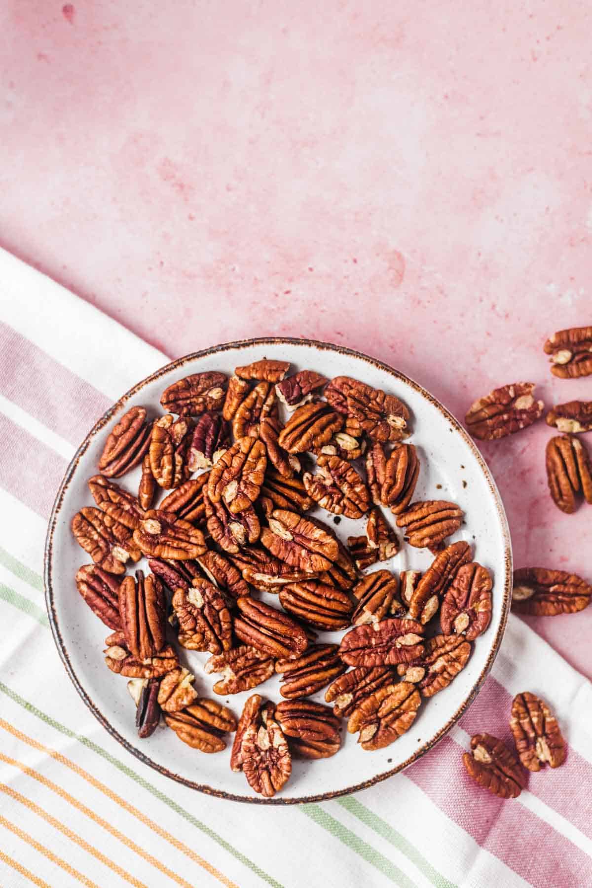 Birds eye view of whole pecans on a white dish.