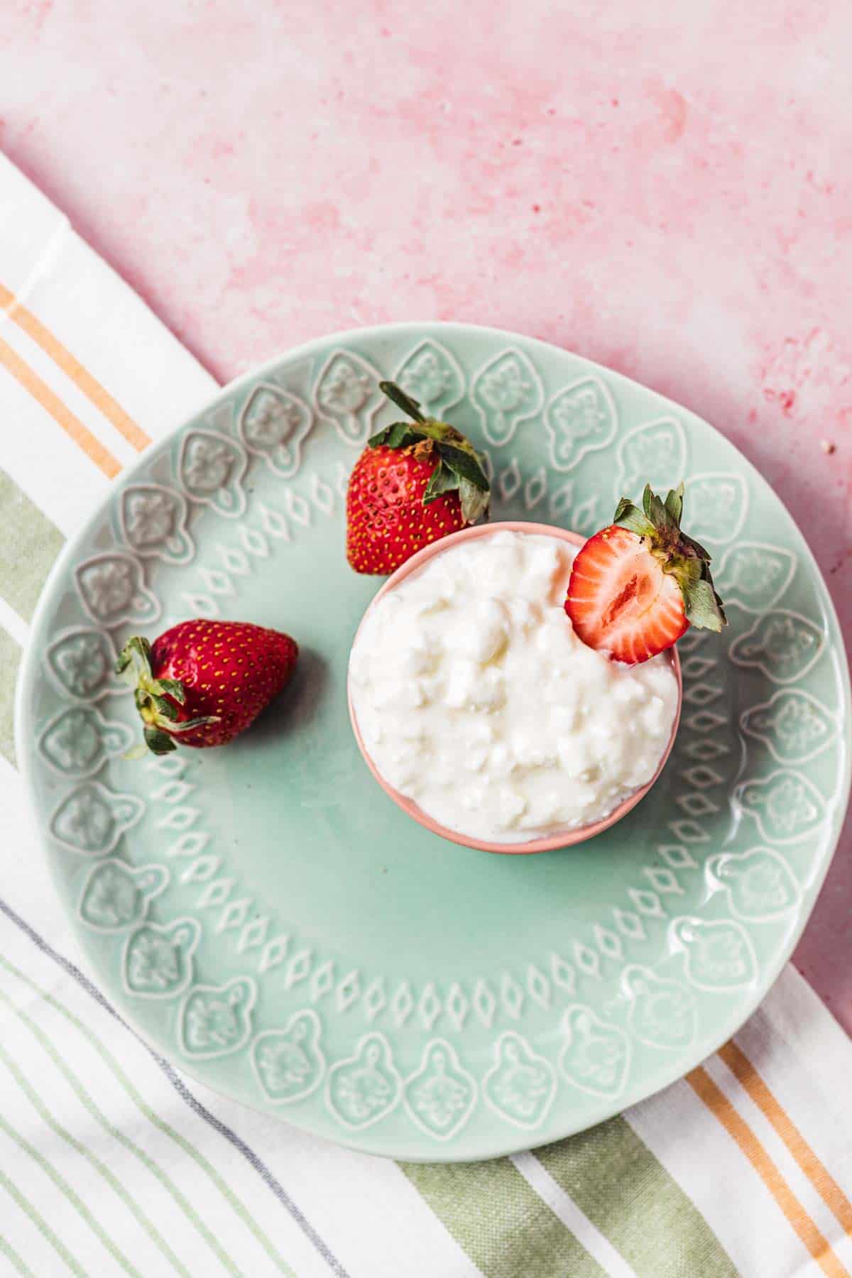 Birds eye view of cottage cheese portioned in a small bowl on a green plate with strawberries on the side.