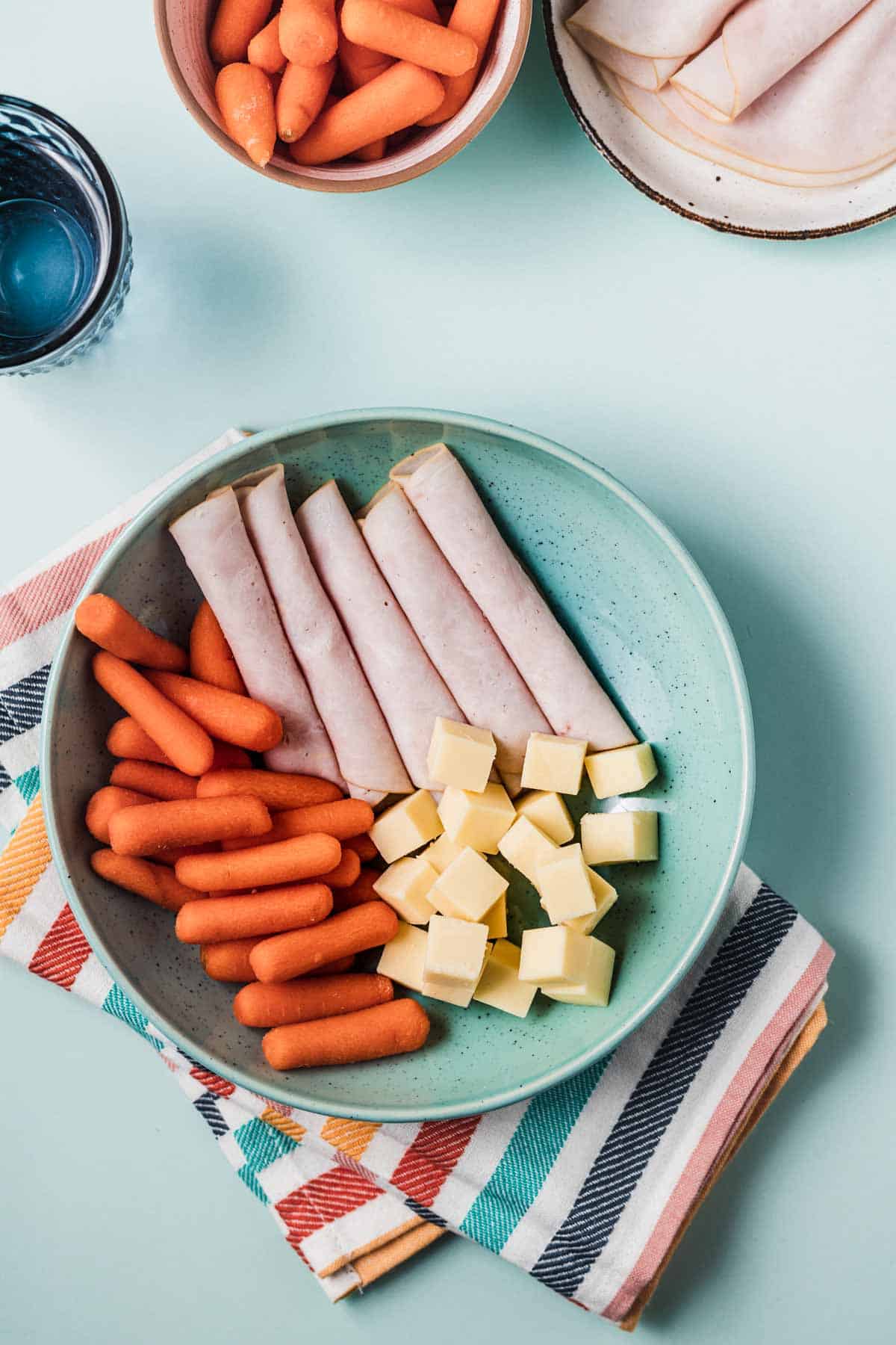 Birds eye view of carrots and cheese plate with turkey slices portioned in a blue bowl.