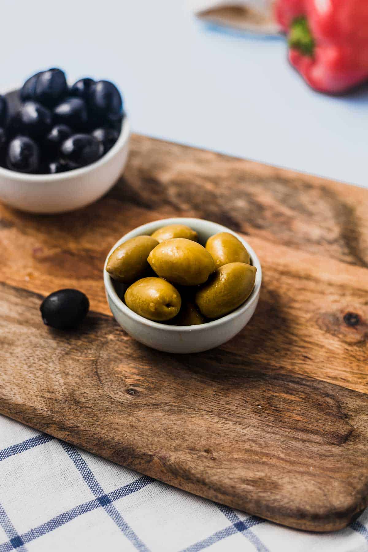 Close up of green olives in a small white ramekin.