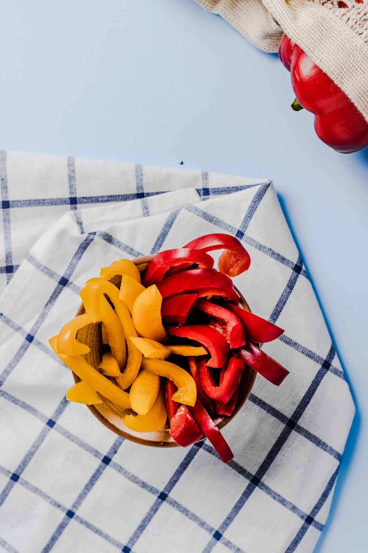 Birds eye view of sliced red and yellow bell peppers in a small bowl.