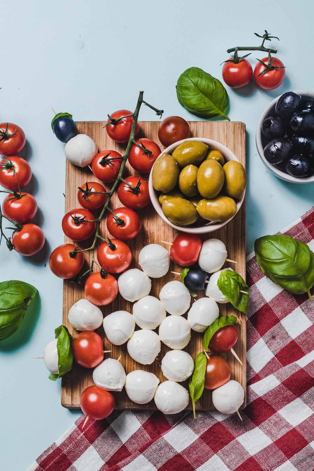 Birds eye view image of hunger crushing snack of cheese balls, tomatoes, and olives on a wooden cutting board.