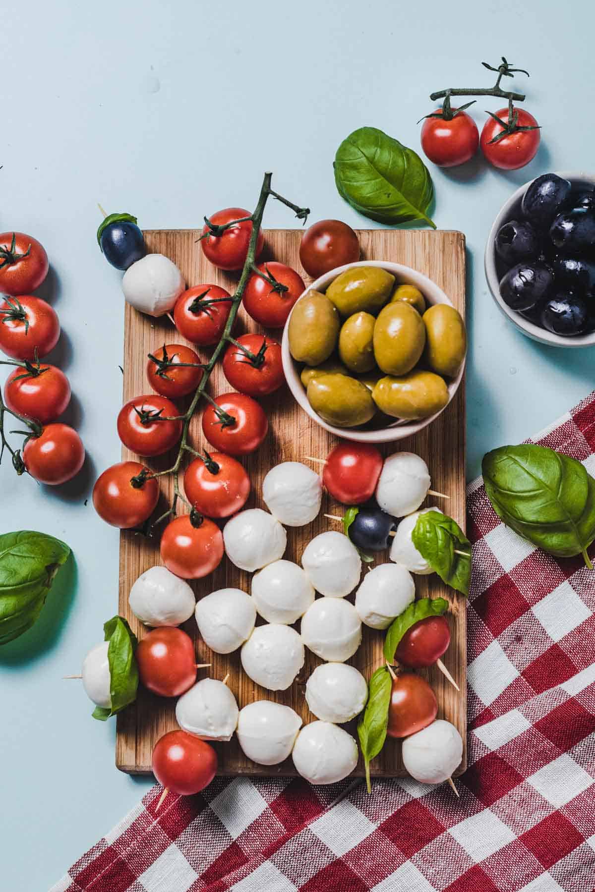 Birds eye view image of hunger crushing snack of cheese balls, tomatoes, and olives on a wooden cutting board. 