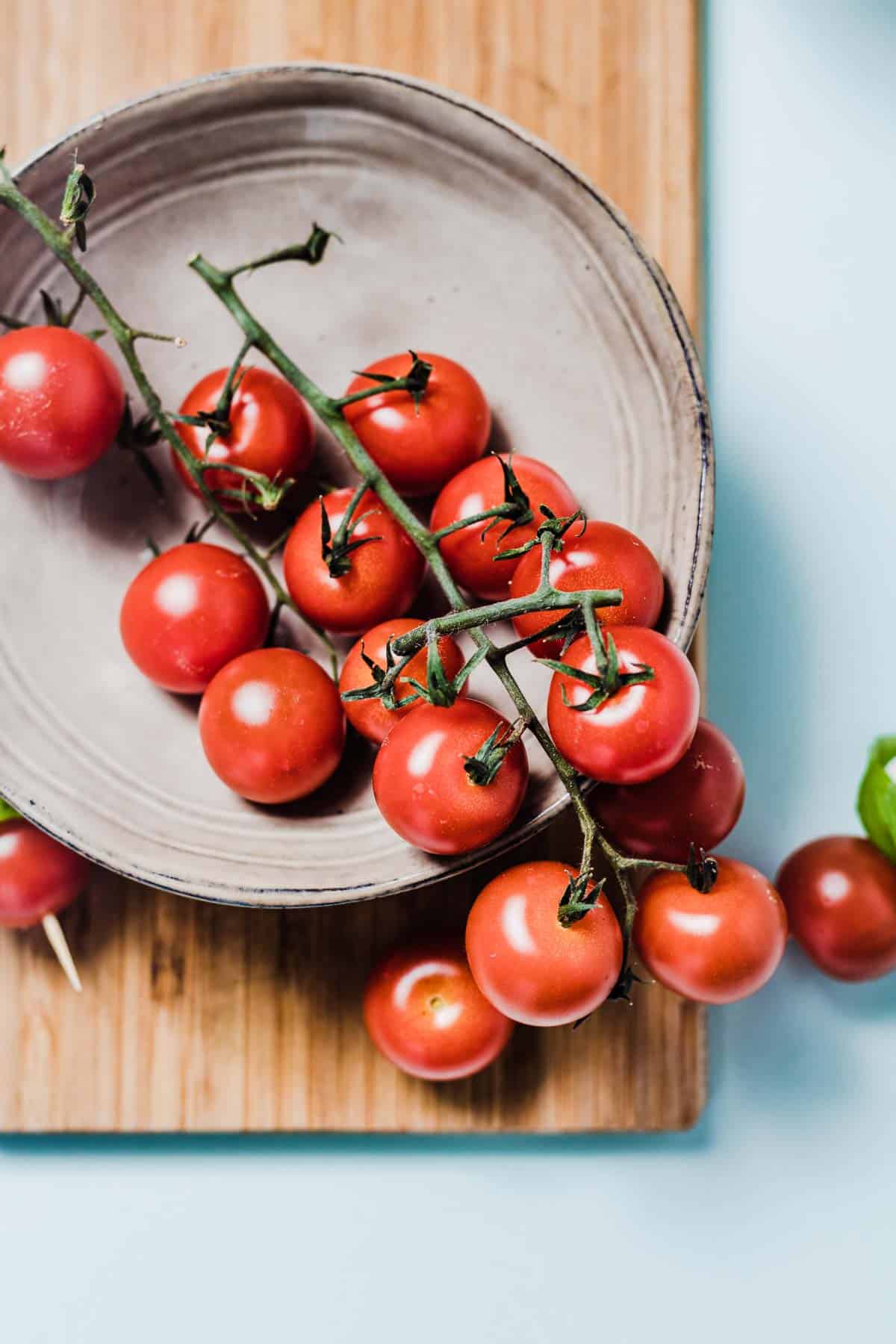 Close up of cherry tomatoes on the vine sitting in a grey bowl.