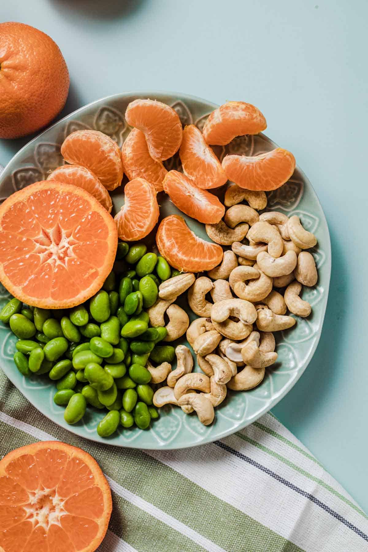 Close up of edamame snack with fruit and nuts on a blue plate.