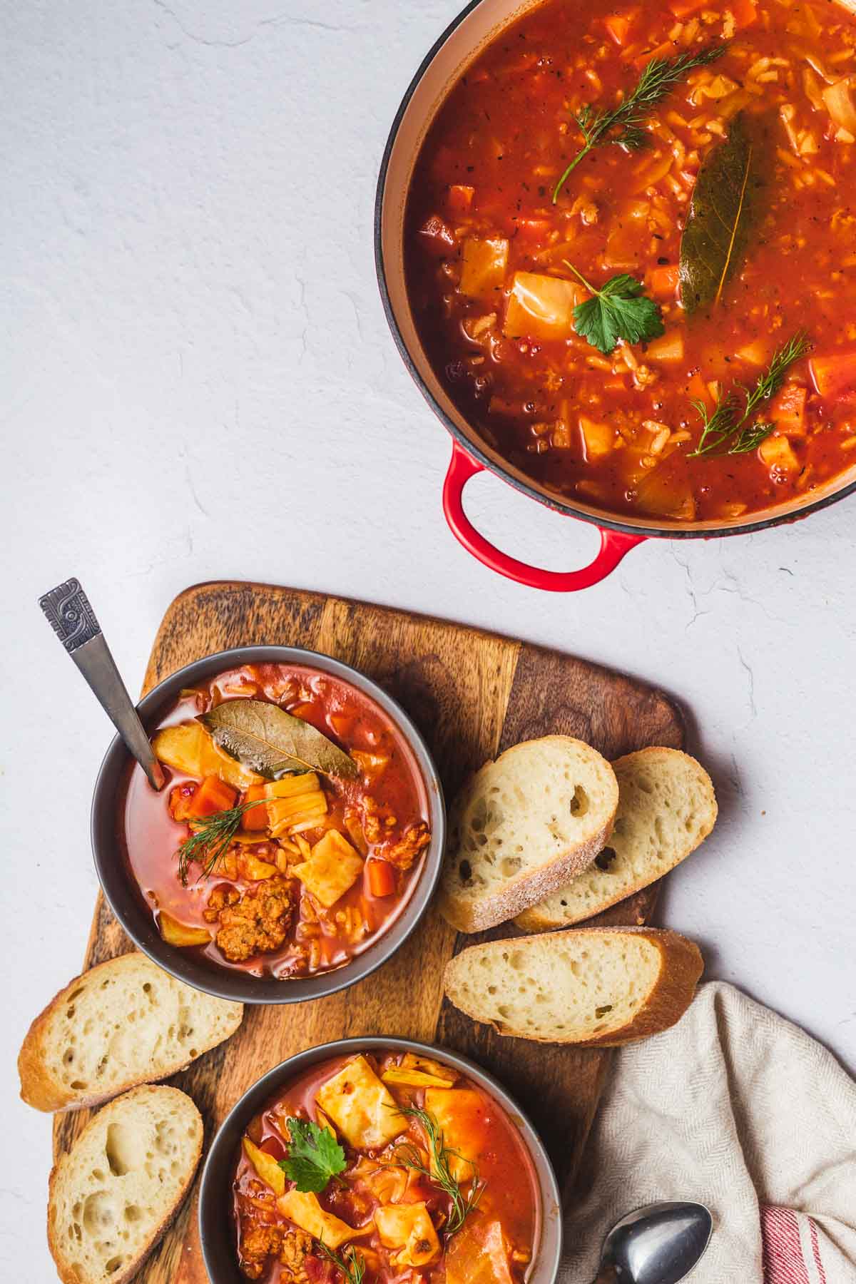 Two bowls of soup on a wooden board served with bread, next to a large pot filled with cabbage soup.